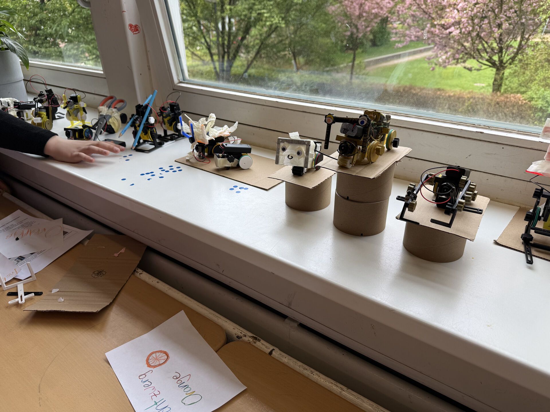 A row of finished robots lined up on a windowsill with cherry blossoms outside
